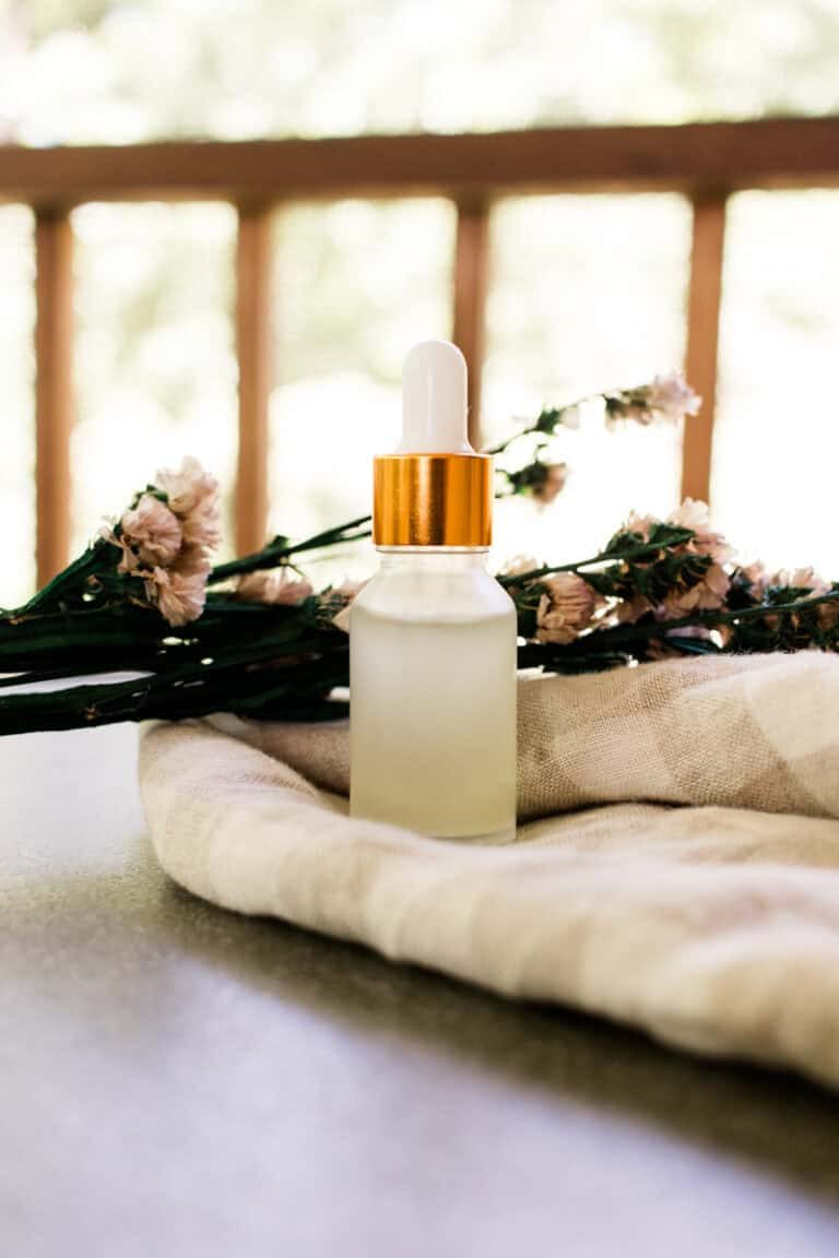 A glass dropper bottle of homemade eye serum on a linen towel with dried flowers in the background.