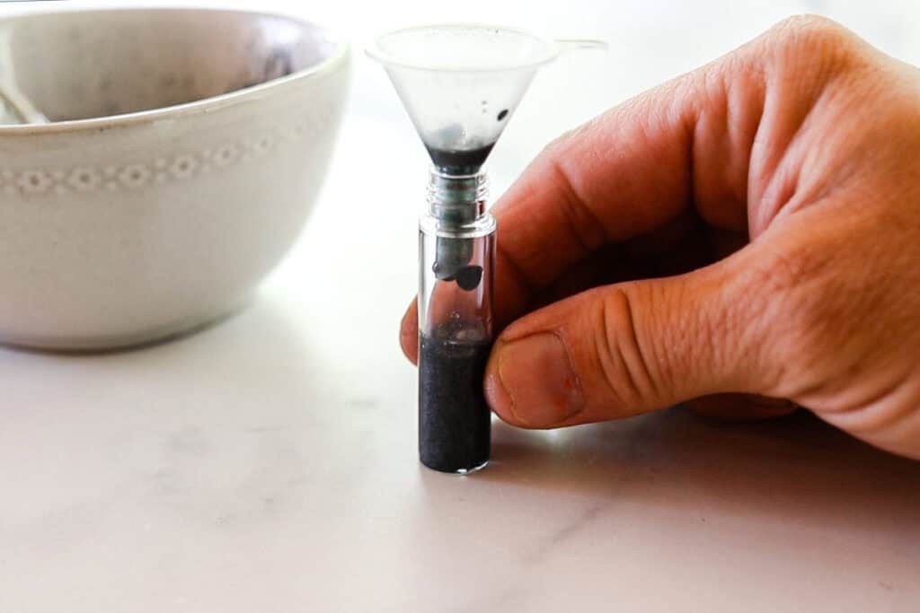 Transferring the homemade eyebrow gel from the bowl into the container for storage. We am using a small plastic funnel to prevent spills.
