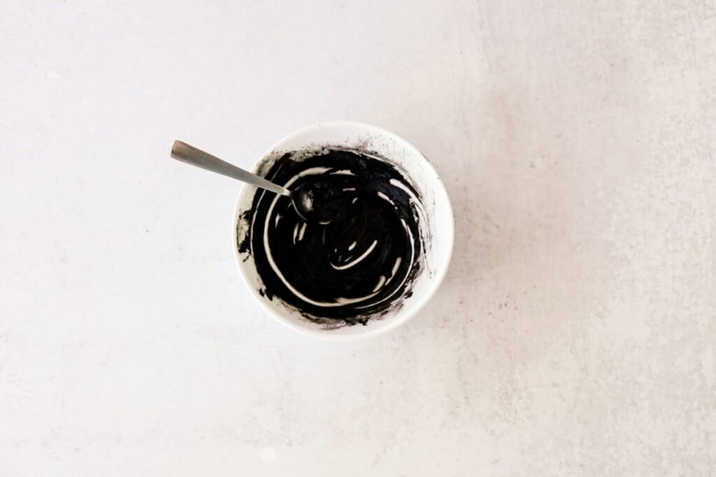 DIY eyebrow tint in a small white bowl with a spoon in it.