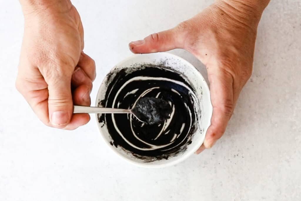 Stirring DIY eyebrow tint in a small bowl to form a thick paste.