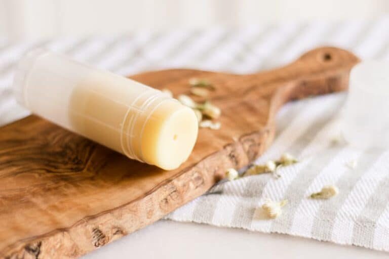 Foot balm stick laying on table with jasmine flowers around it.