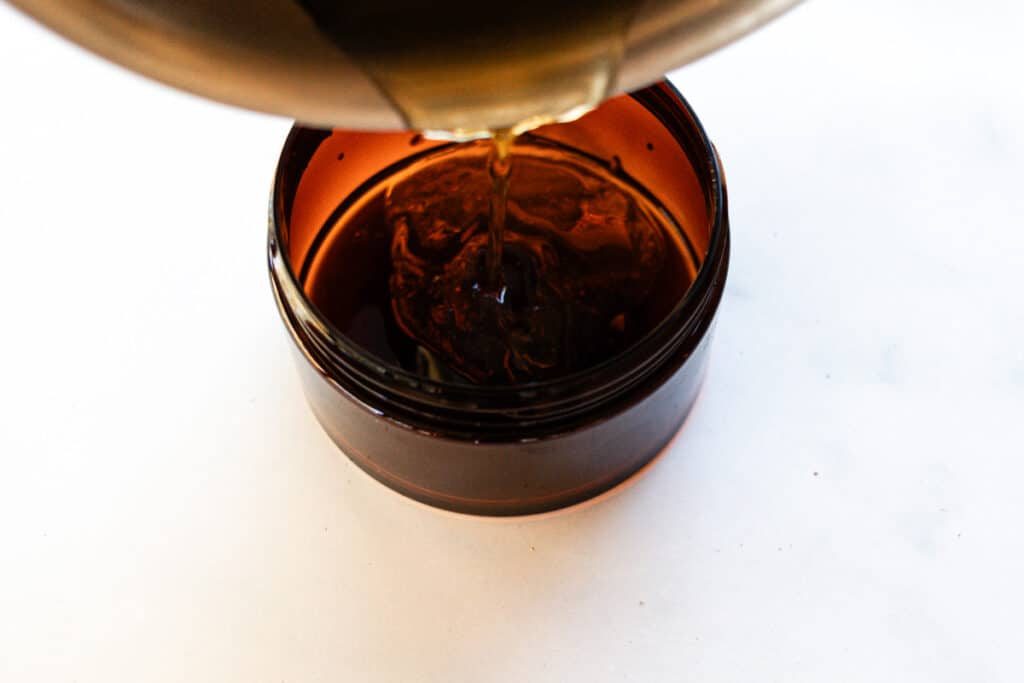 Pouring the melted foot mask ingredients out of the saucepan into the container.