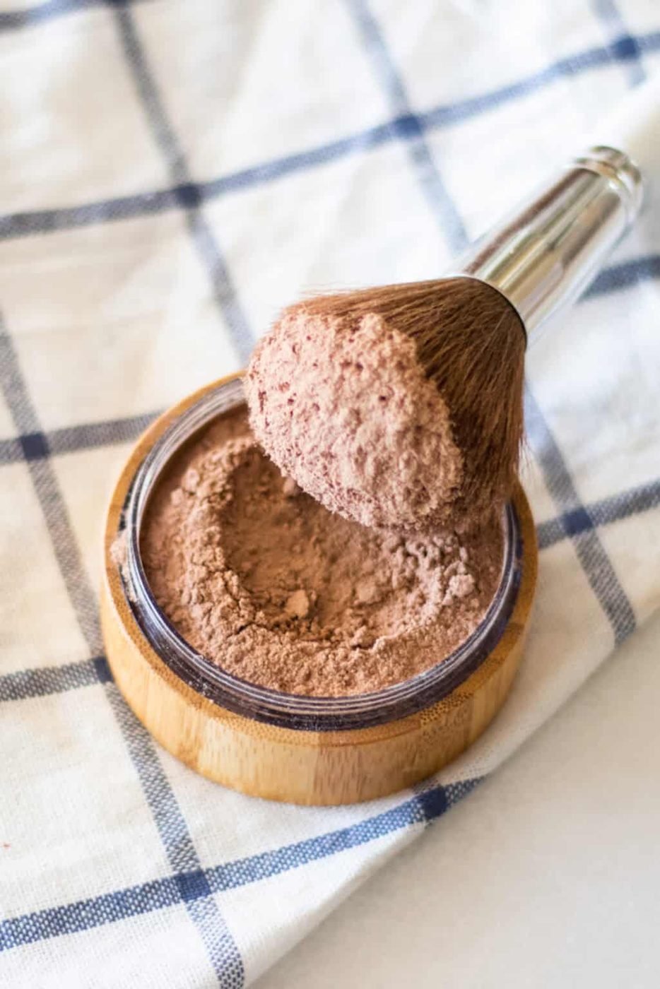 Dipping a makeup brush in a container of homemade foundation.