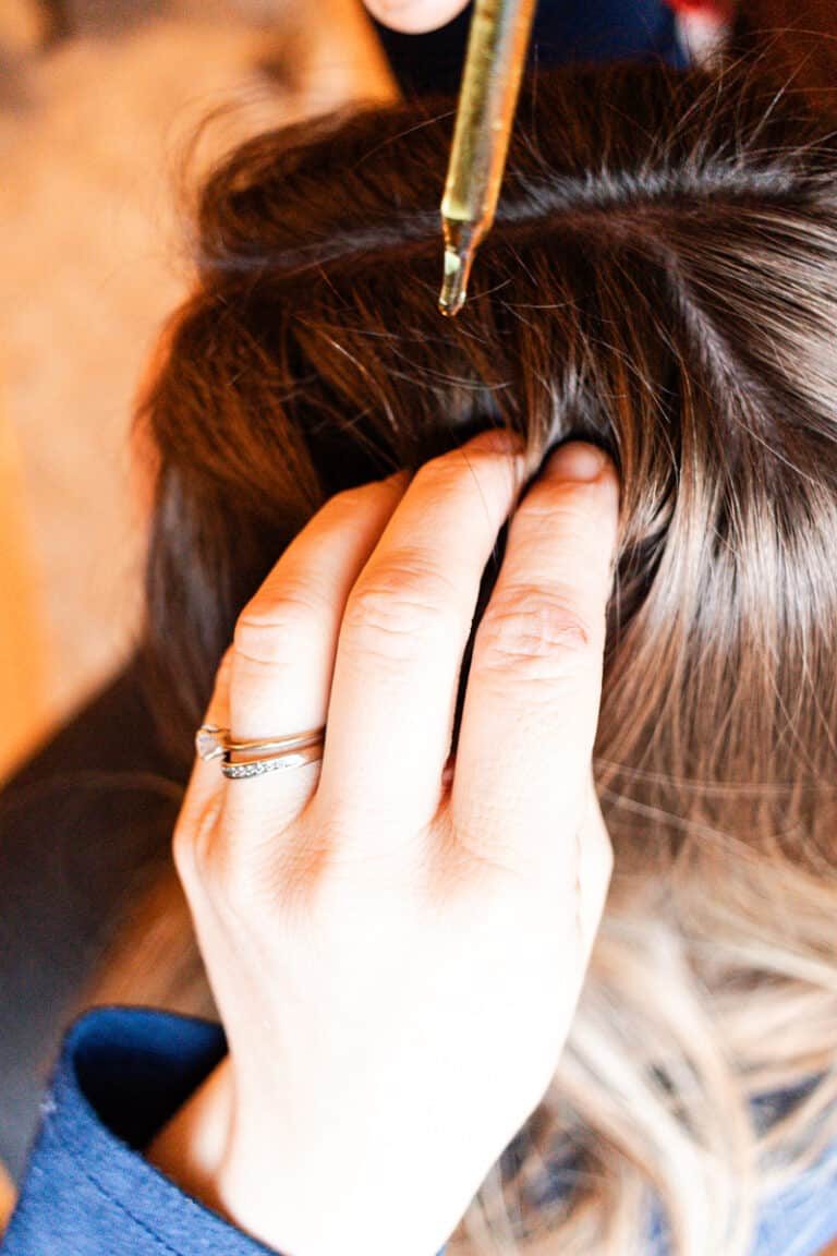 Using a dropper to apply the homemade hair growth oil to our hair.