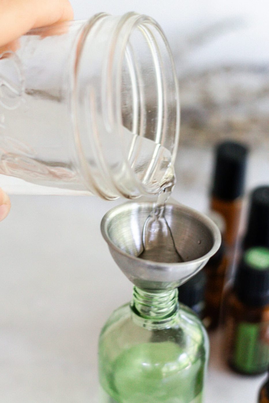 Pouring water into a glass spray bottle with a small metal funnel.