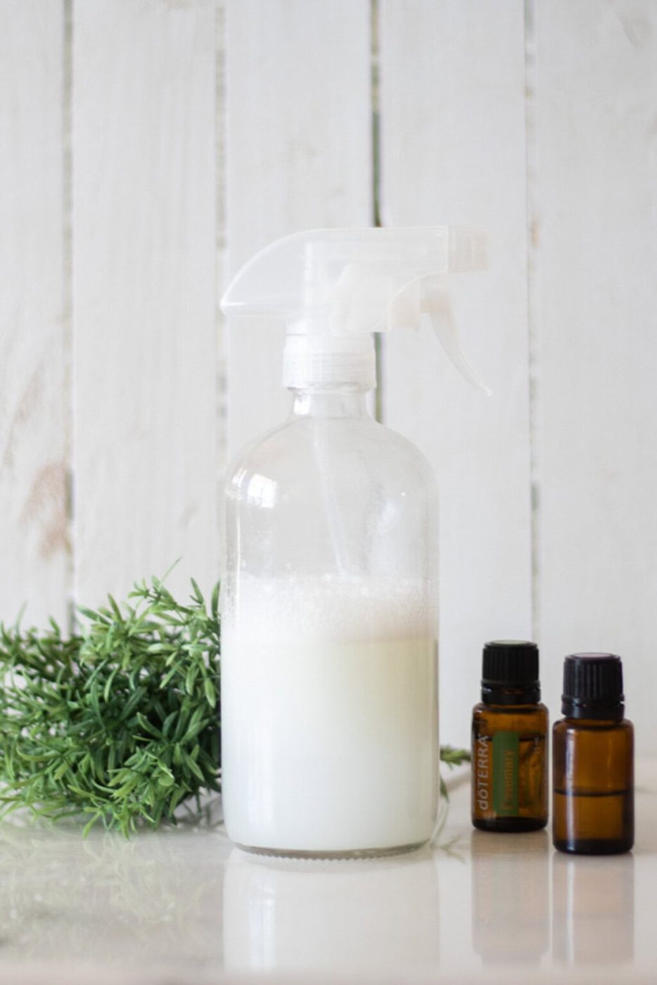 A bottle of hair heat protectant with essential oils and a plant in the background.
