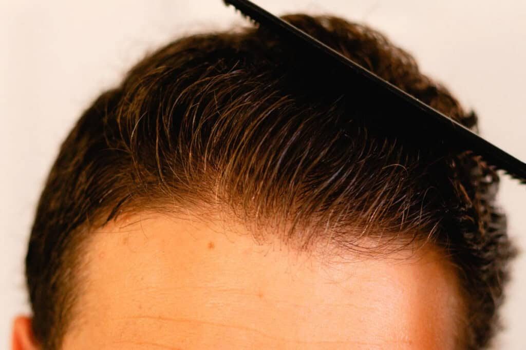 The top of a man's head with hair pomade being combed through the hair.