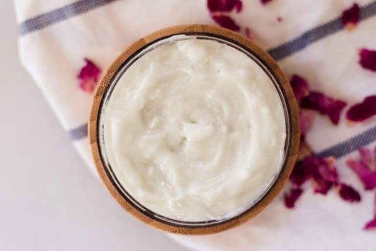 Homemade styling hair cream in small container with rose petals around it.