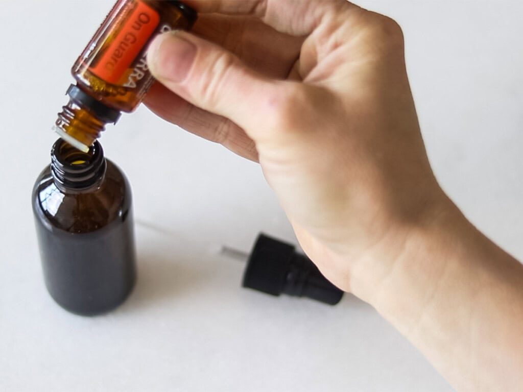 Dropping essential oils into a glass spray bottle.