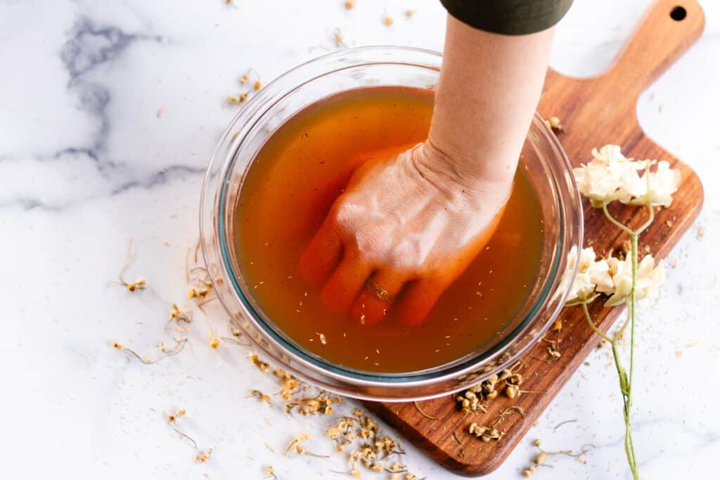 Submerging our hand into a homemade hand soak recipe on a marble table top.