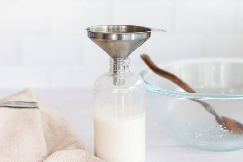 A glass bottle with a metal funnel in the top, full of DIY leave-in conditioner.
