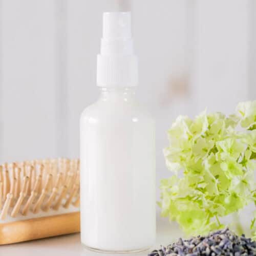 A bottle of leave-in conditioner next to dried flowers and a hair brush.