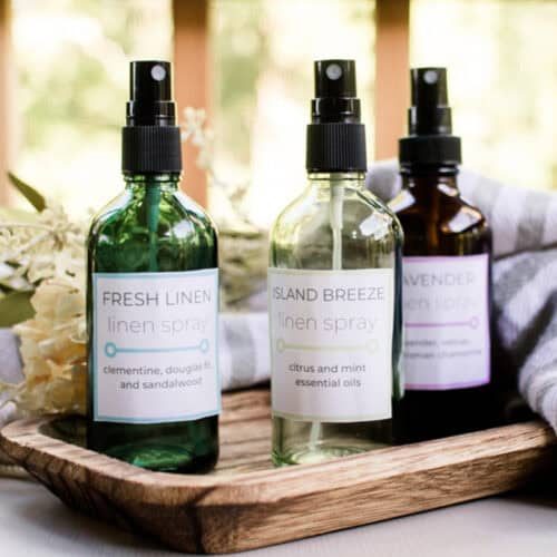 Homemade linen sprays scented with essential oils on a wooden tray with homemade labels.