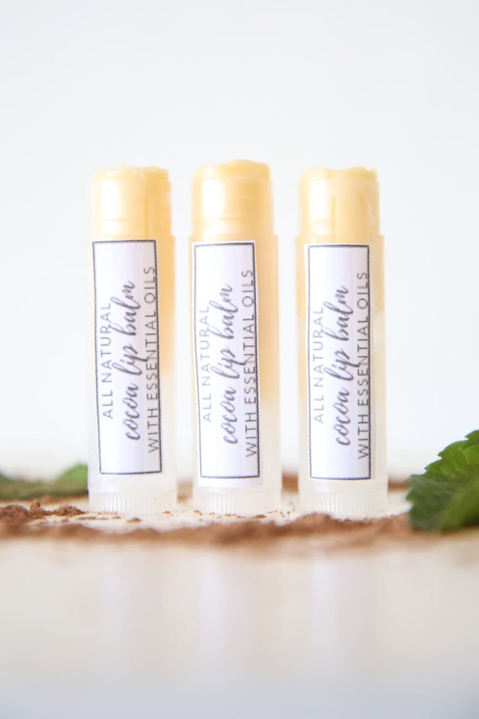3 DIY lip balms in clear tubes with homemade labels on white marble.