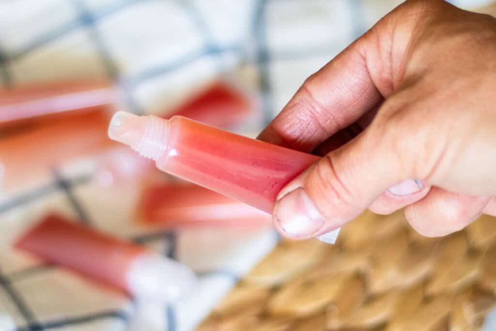 Holding a tube of pink lip gloss.