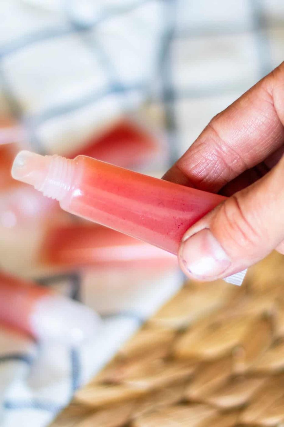 Holding a tube of DIY lip gloss over other tubes on a towel.