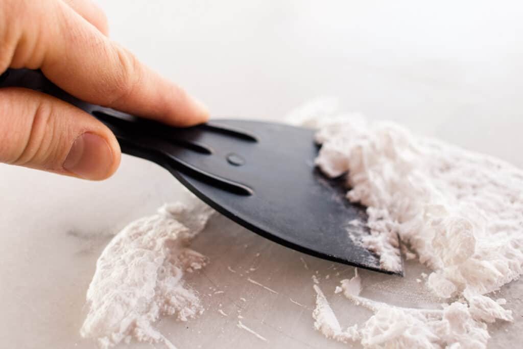 Scraping off baking soda from a white marble surface.