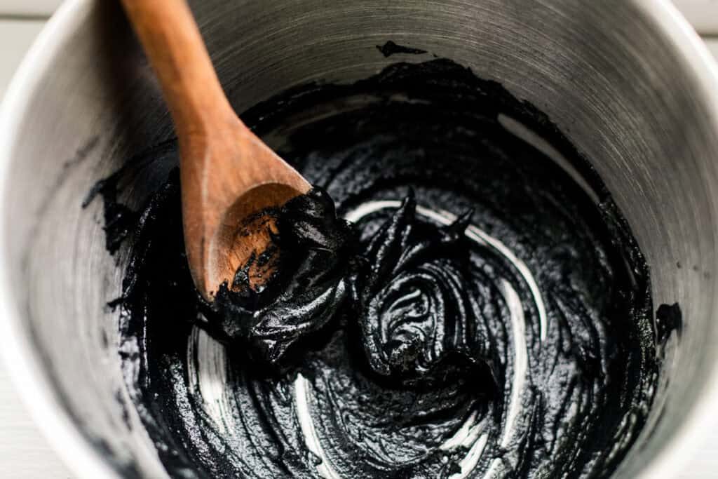 Stirring the homemade mascara until its well combined and creamy with a wooden spoon.