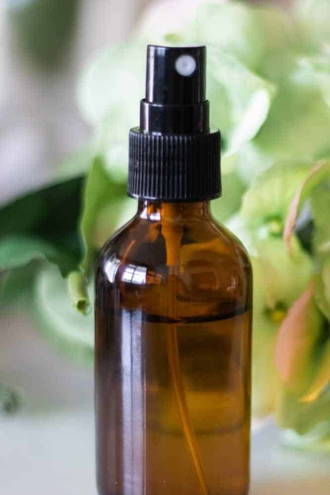 Mattress spray in amber glass spray bottle with green flowers behind it.