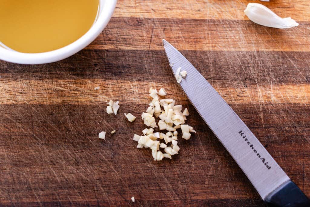 Dicing up a clove of garlic on a wooden cutting board.