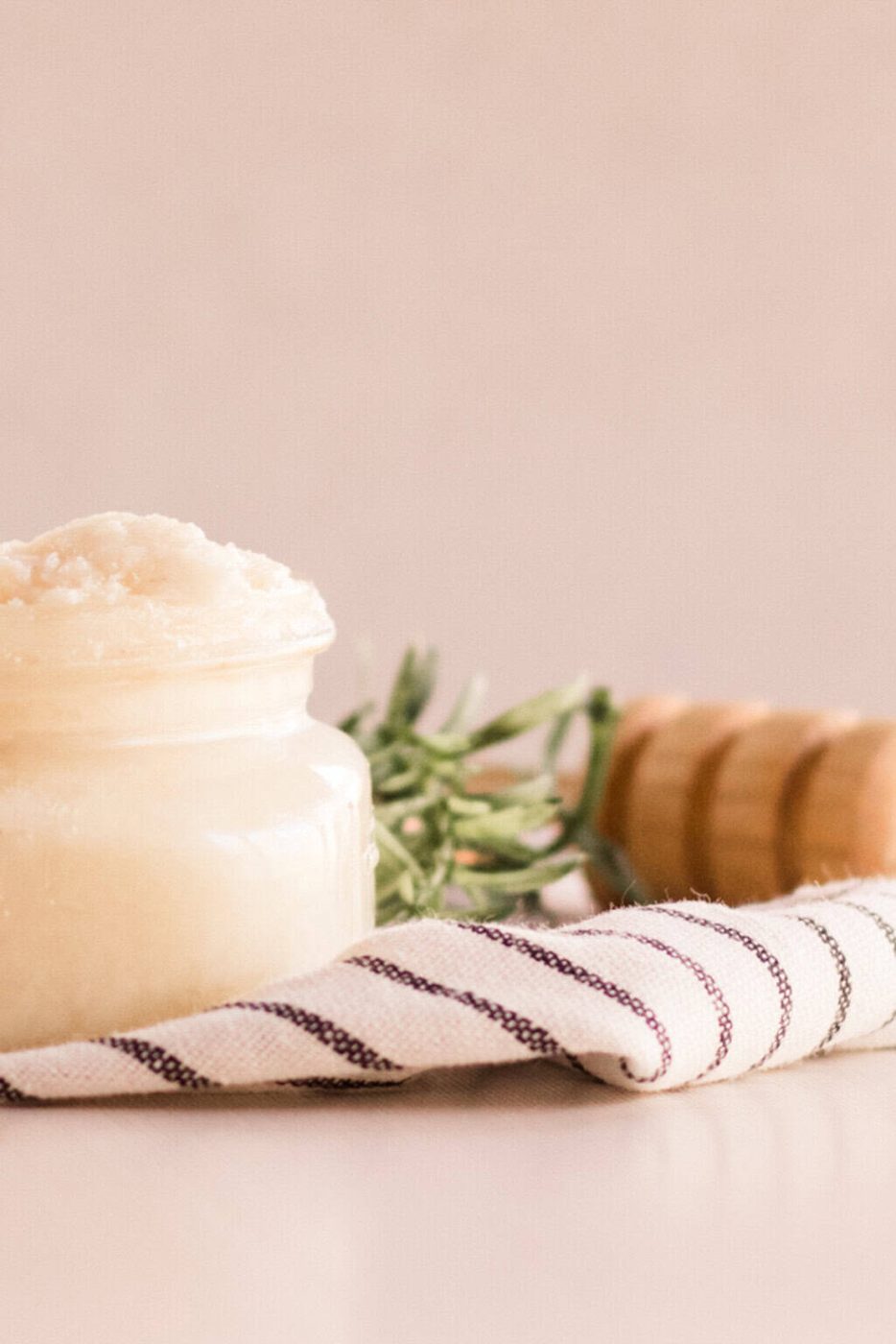 A jar of homemade protein hair mask on a striped towel with a honey stick behind it.