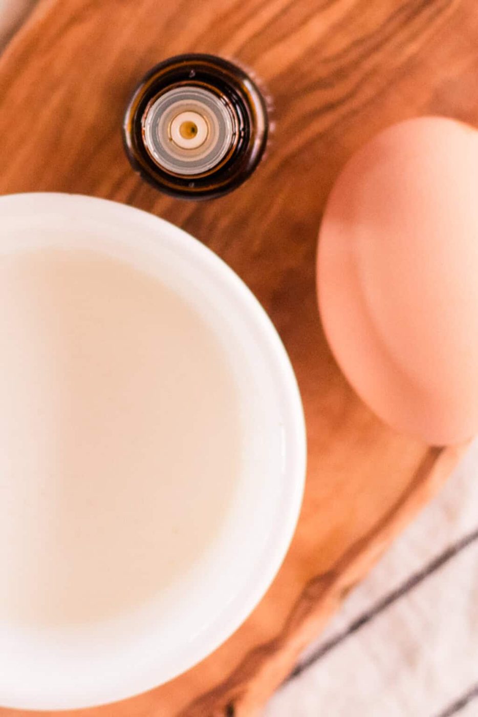 A bowl of yogurt, an egg, and a bottle of essential oil sitting on a wooden cutting board.