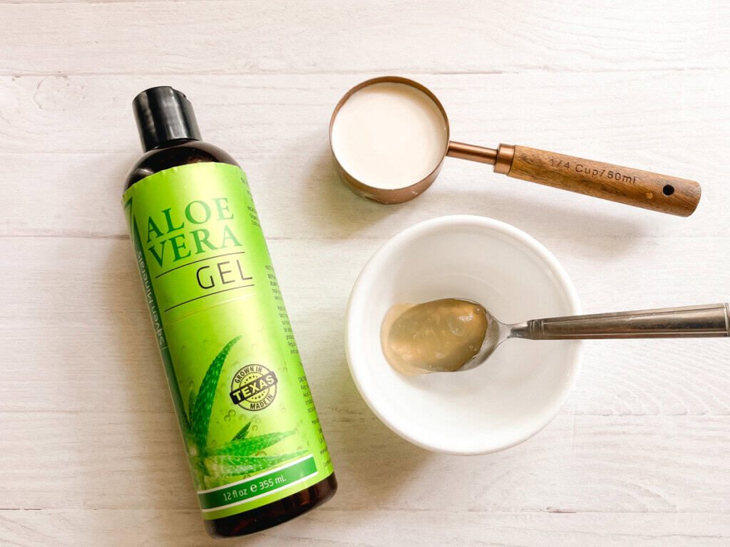 A bottle of aloe vera with a measuring cup of coconut milk, a bowl, and a spoonful of aloe vera.