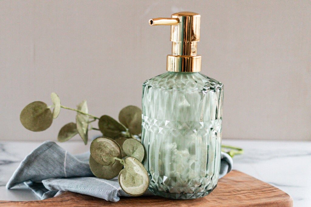 A green glass pump bottle of lotion on a wooden board with eucalyptus leaves.