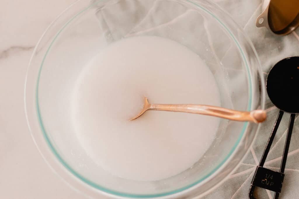 A glass bowl with soap scum mixture and a spoon in it.