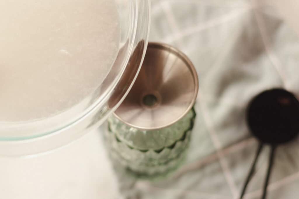 Pouring soap scum remover into a green glass spray bottle.