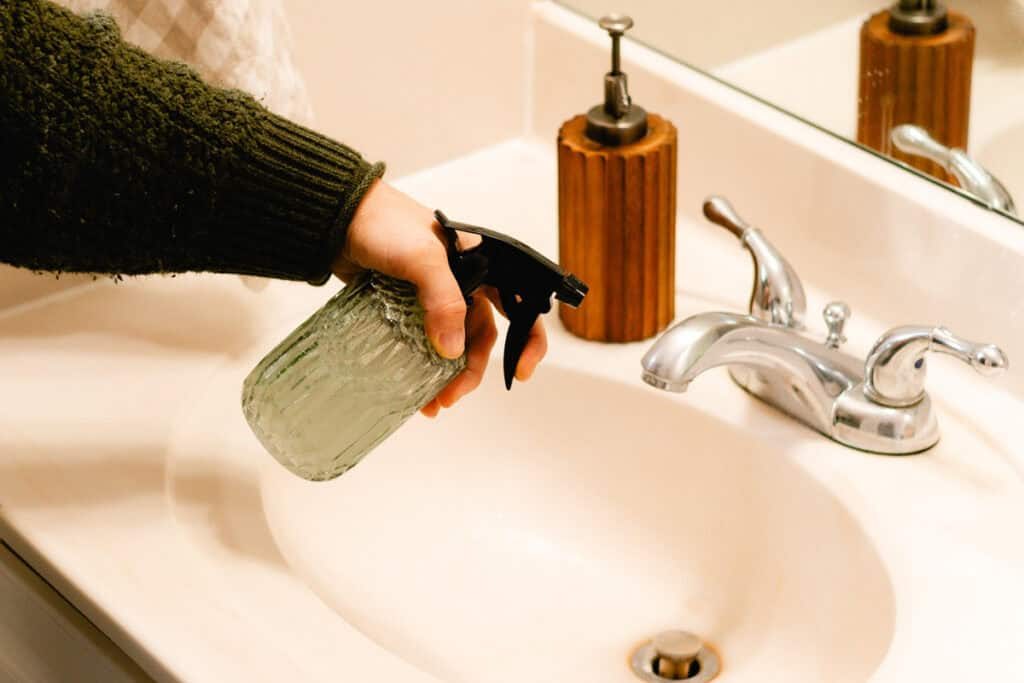 Spraying soap scum remover onto a bathroom sink.