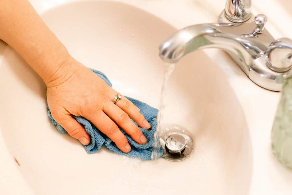 Rinsing a bathroom sink with water and a microfiber cloth.