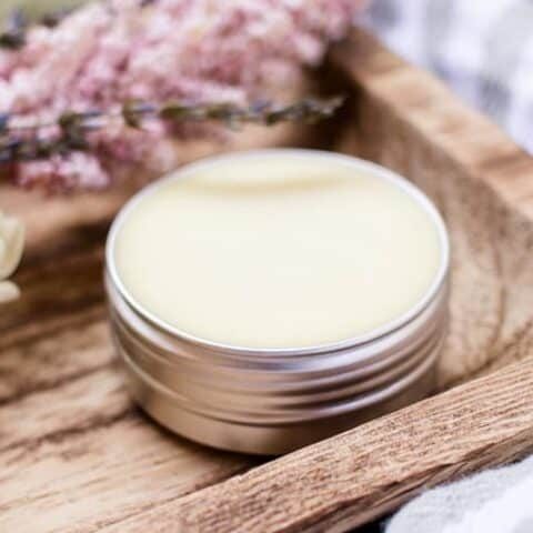 A solid perfume in a small metal tin stored on a wooden shelf.