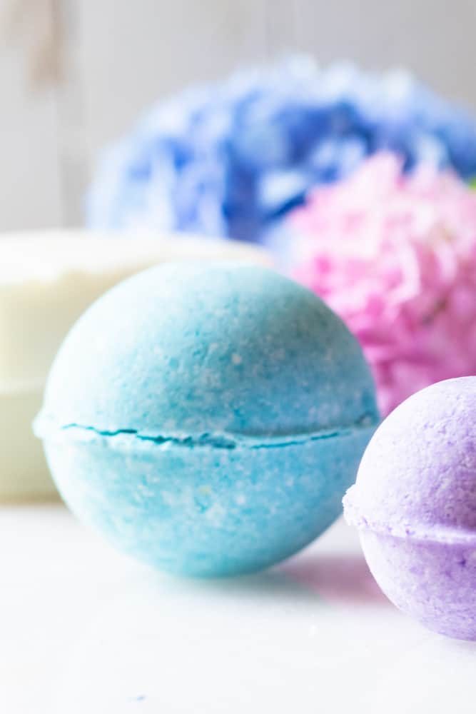 Brightly colored bath bombs with pink and blue flowers behind them.