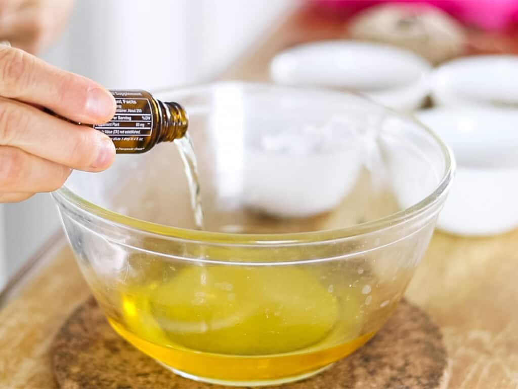 Pouring essential oils into a mixing bowl with melted wax.