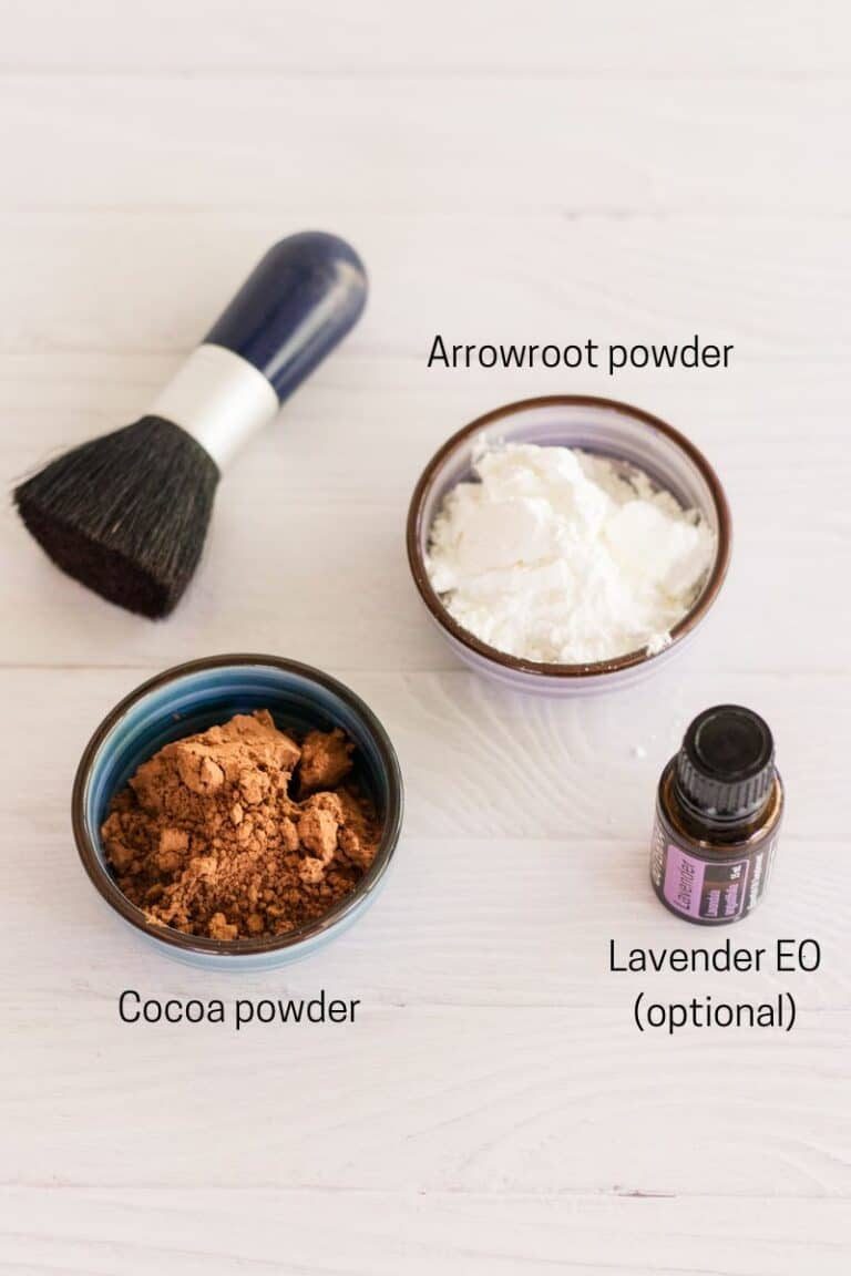 Dry shampoo ingredients: cocoa powder, arrowroot powder, lavender essential oil next to a makeup brush.