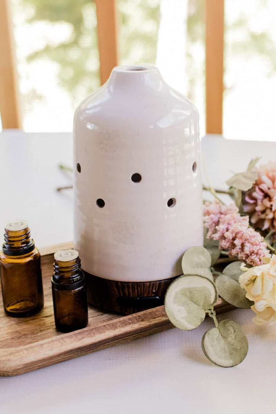White and brown diffuser sitting on a corner table near a window with decorative flowers.