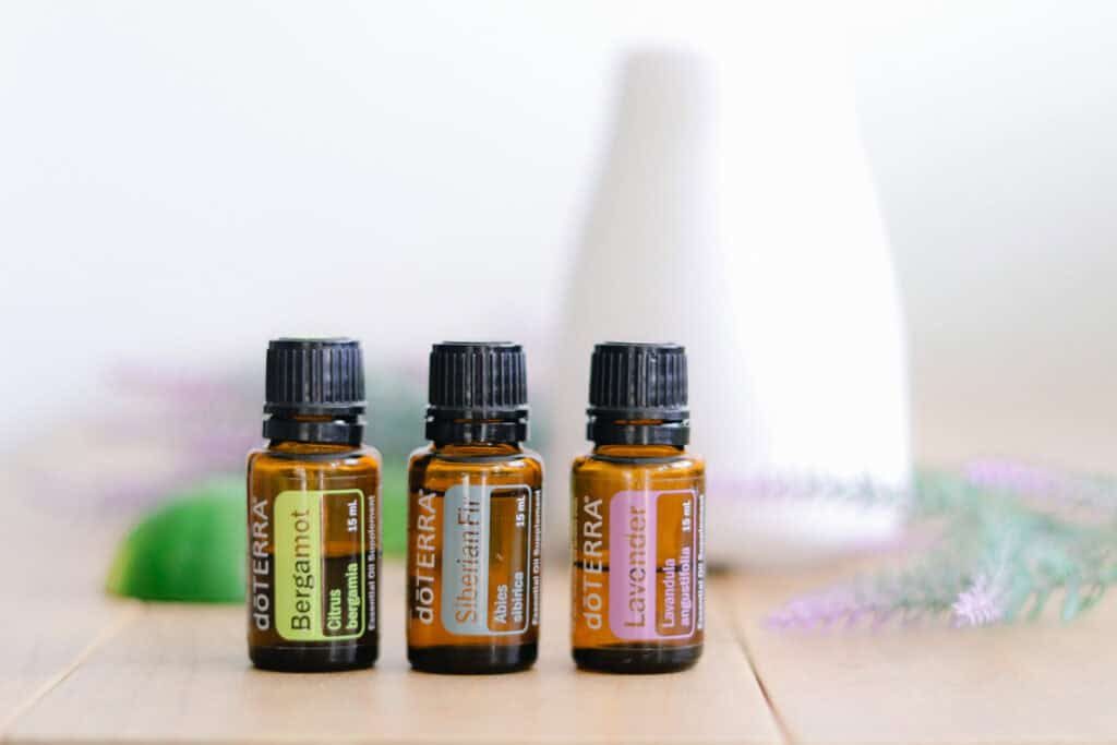 Three essential oil bottles on a wooden table with a white diffuser behind them.