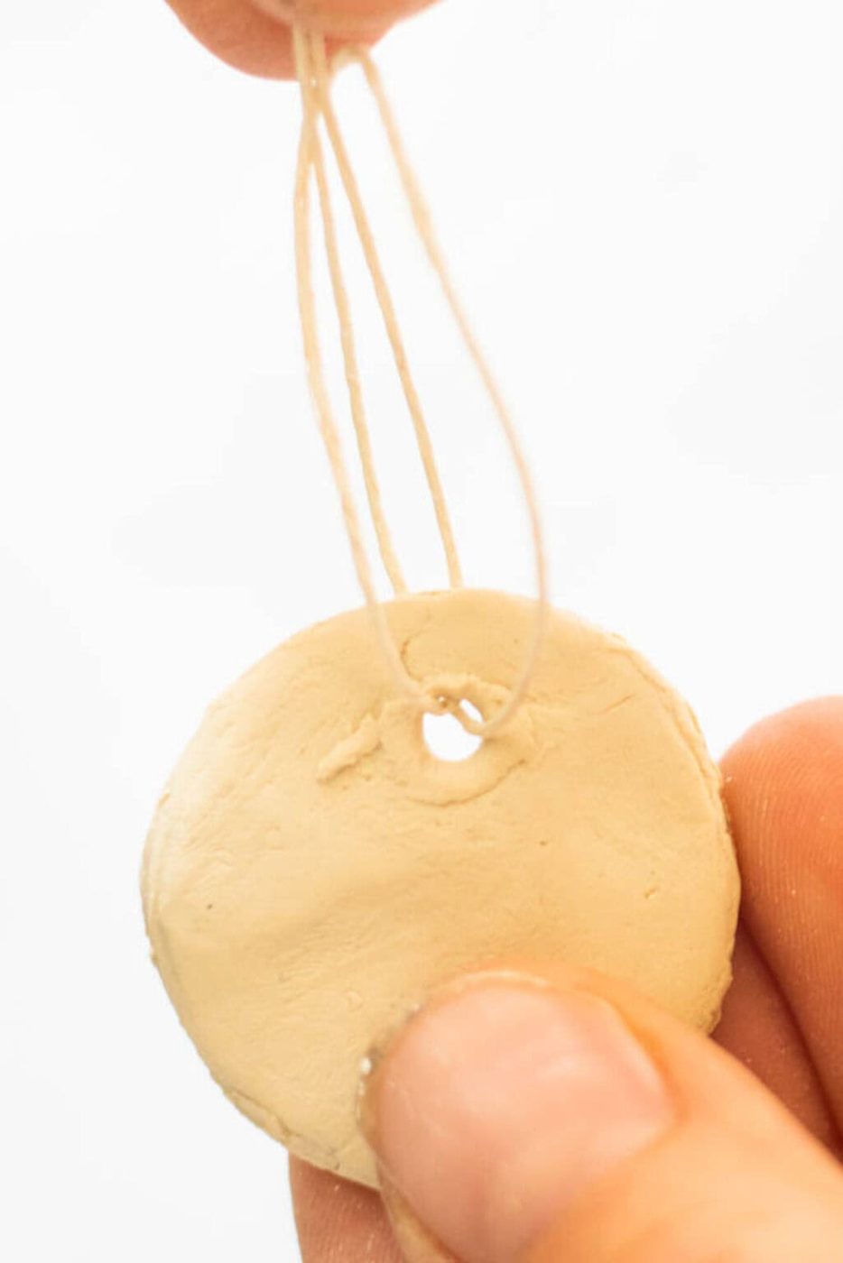 Stringing a piece of twine through a clay pendant with a hole in the top.