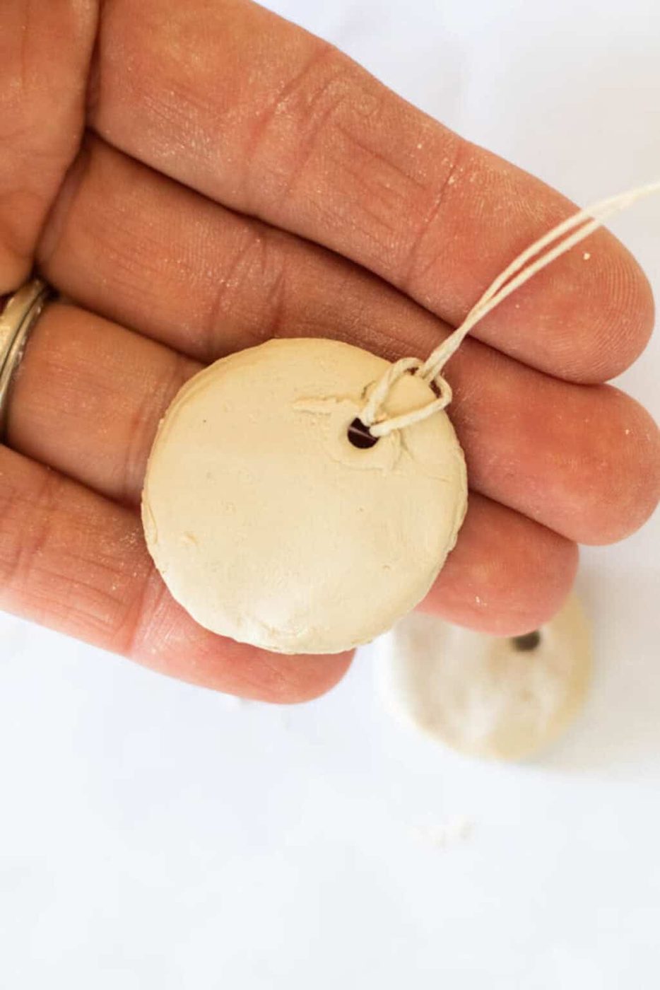 Holding an air dry clay necklace out after running the string through it.
