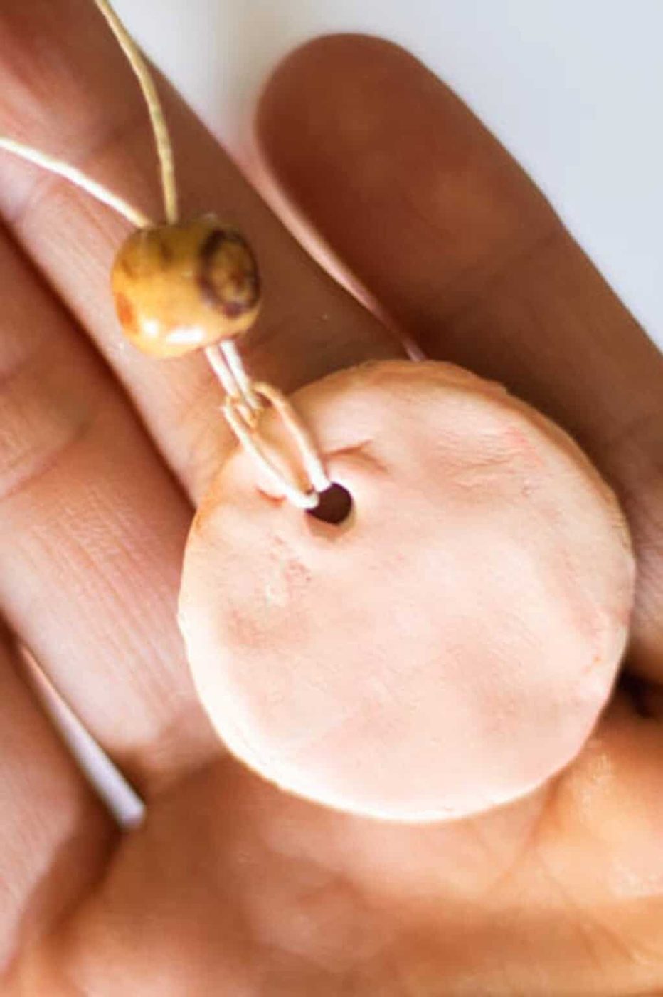 A hand holding a clay diffuser necklace with twine and a bead threaded through it.