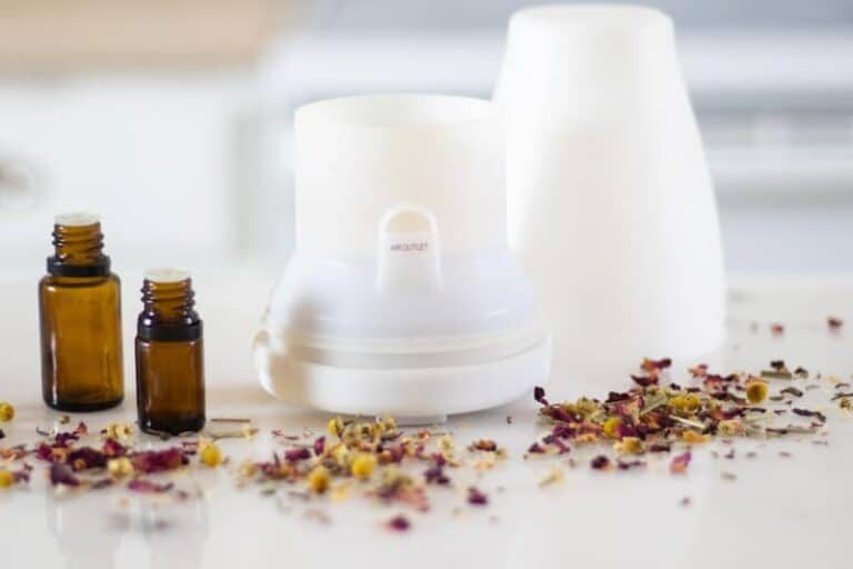 White essential oil diffuser on marble table with dried petals around it.