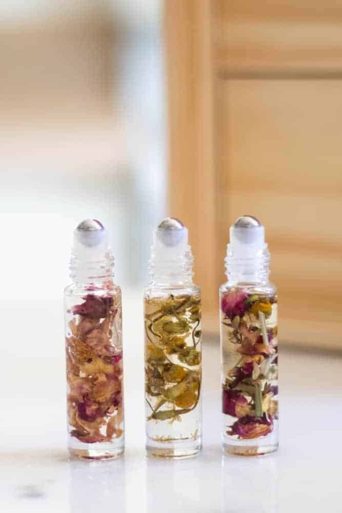 Three essential oil roller bottles that are infused with flowers standing on white marble.