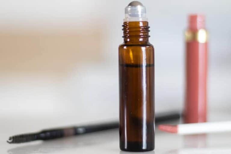 DIY eyebrow growth roller bottle with pink lip gloss in background.