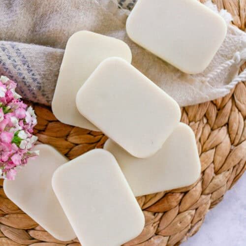 Soap bars for the face on a wicker mat with purple flowers next to it.