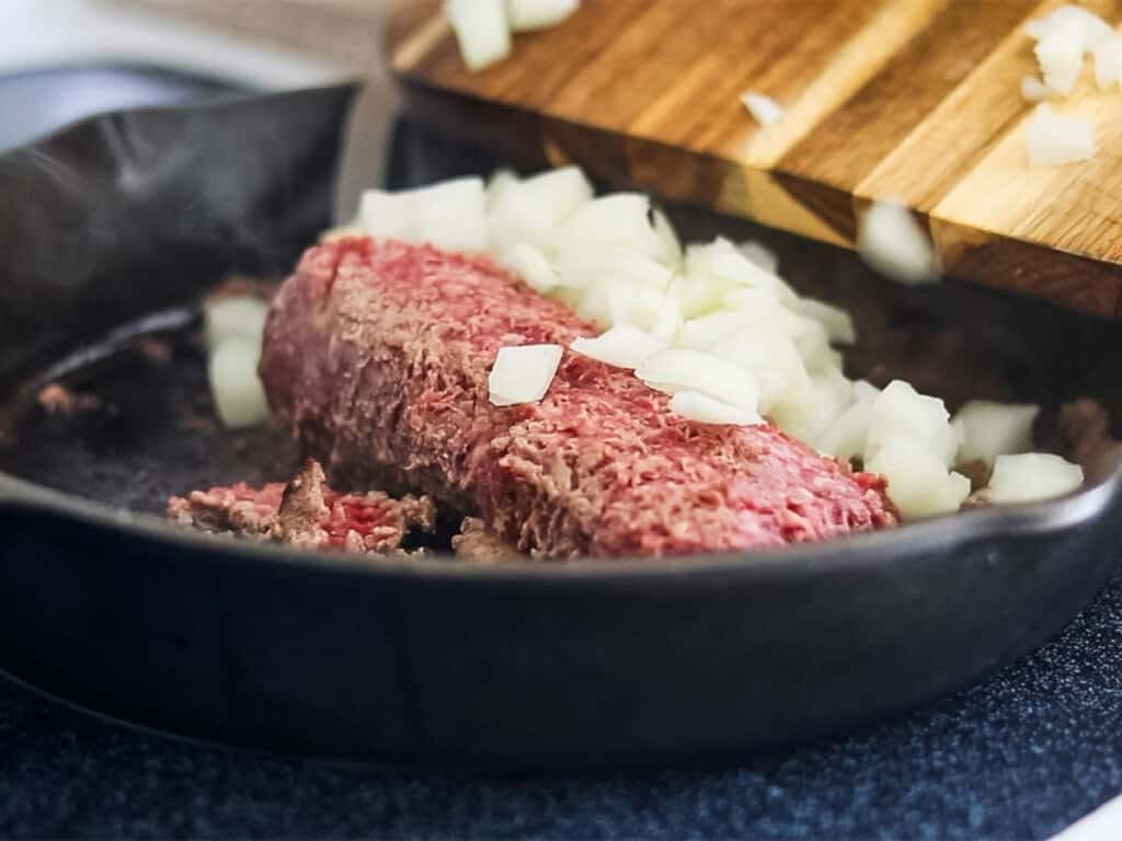 Browning ground beef with onions in a cast iron skillet.