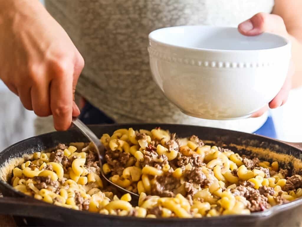 Scooping gluten-free hamburger helper into a white dinner bowl.