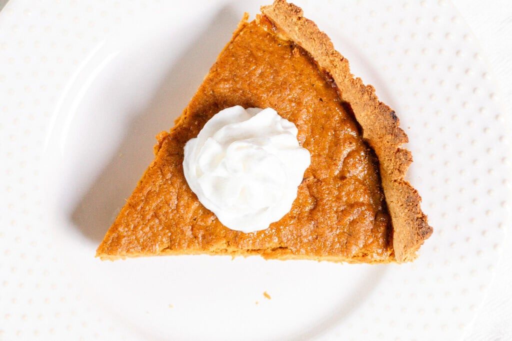 A slice of healthy pumpkin pie with coconut whipped cream on top.