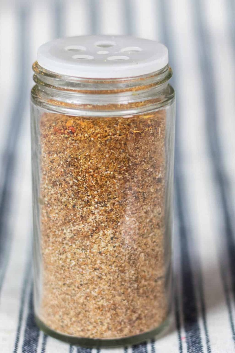 A jar of homemade gluten-free taco seasoning on a striped tablecloth.