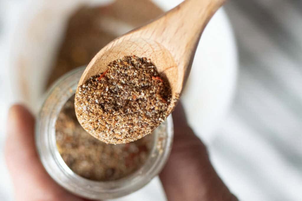 A wooden measuring spoon scooping homemade taco seasoning out of a jar.